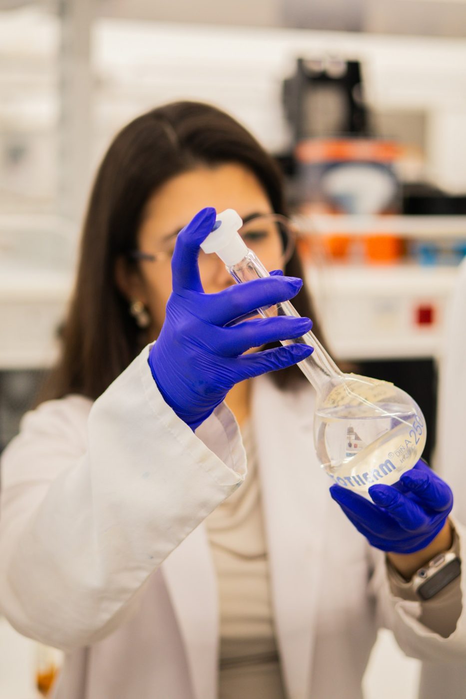 Chemist in a lab coat and gloves examining a flask