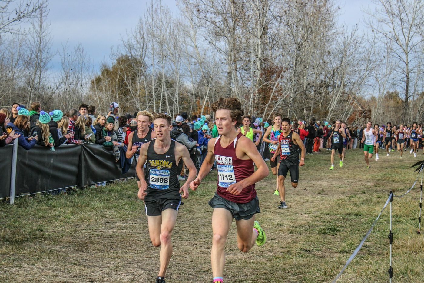 High school runners racing on a grass cross-country course lined with spectators